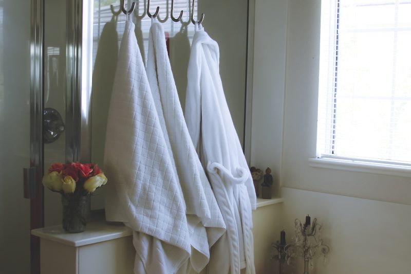 White towels and robes hanging on hooks beside a bright bathroom window