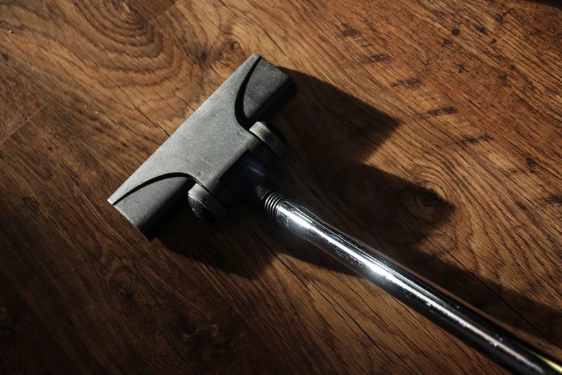 A vacuum cleaner head with a chrome wand on a dark hardwood floor